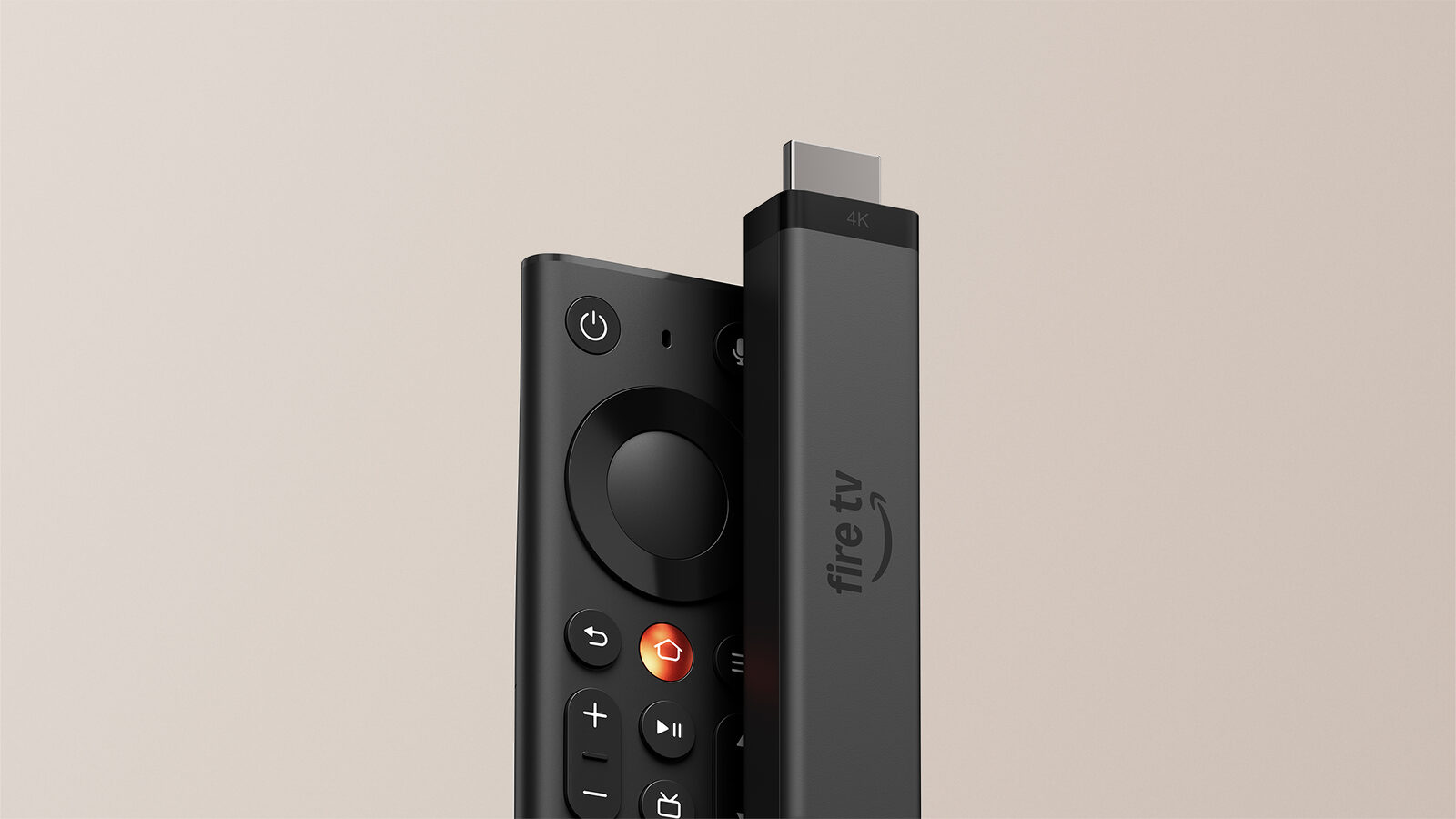 Der neue Fire TV Stick 4K in Dunkelgrau neben der neuen Fire-TV-Fernbedienung mit orangefarbener Home-Taste vor beigem Hintergrund
