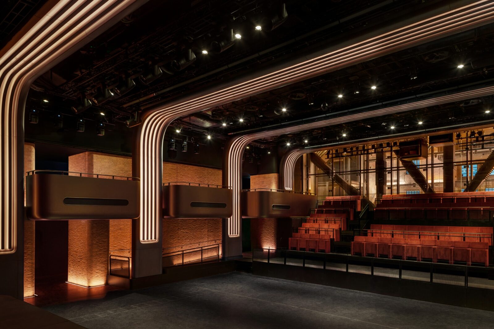 Apple Music Hall'un kırmızı koltuklu, bronz balkonlu ve ışıklı kemerli konser salonu