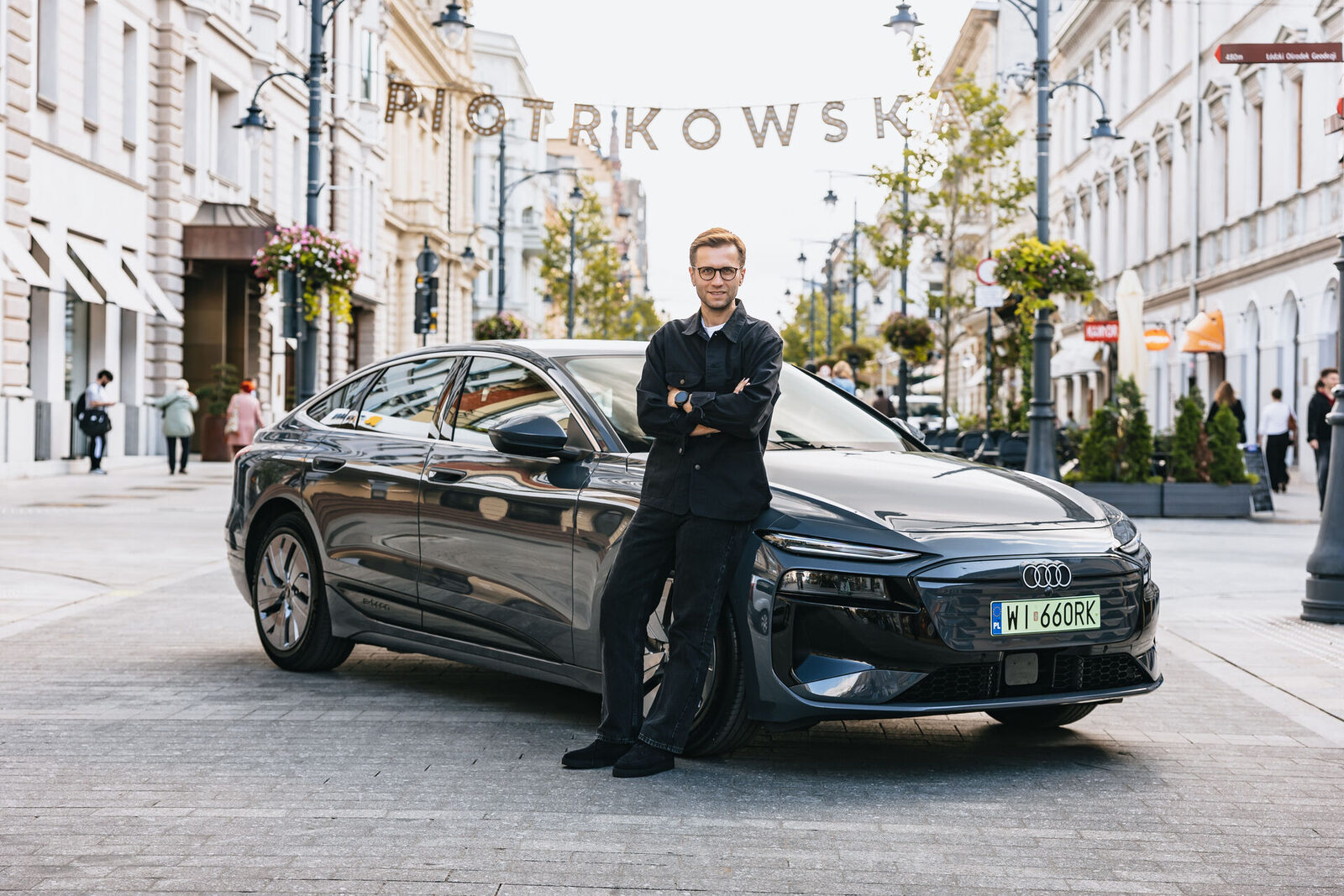 Rallyefahrer Miko Marczyk steht vor einem dunkelgrauen Audi A6 Sportback e-tron in einer Fußgängerzone