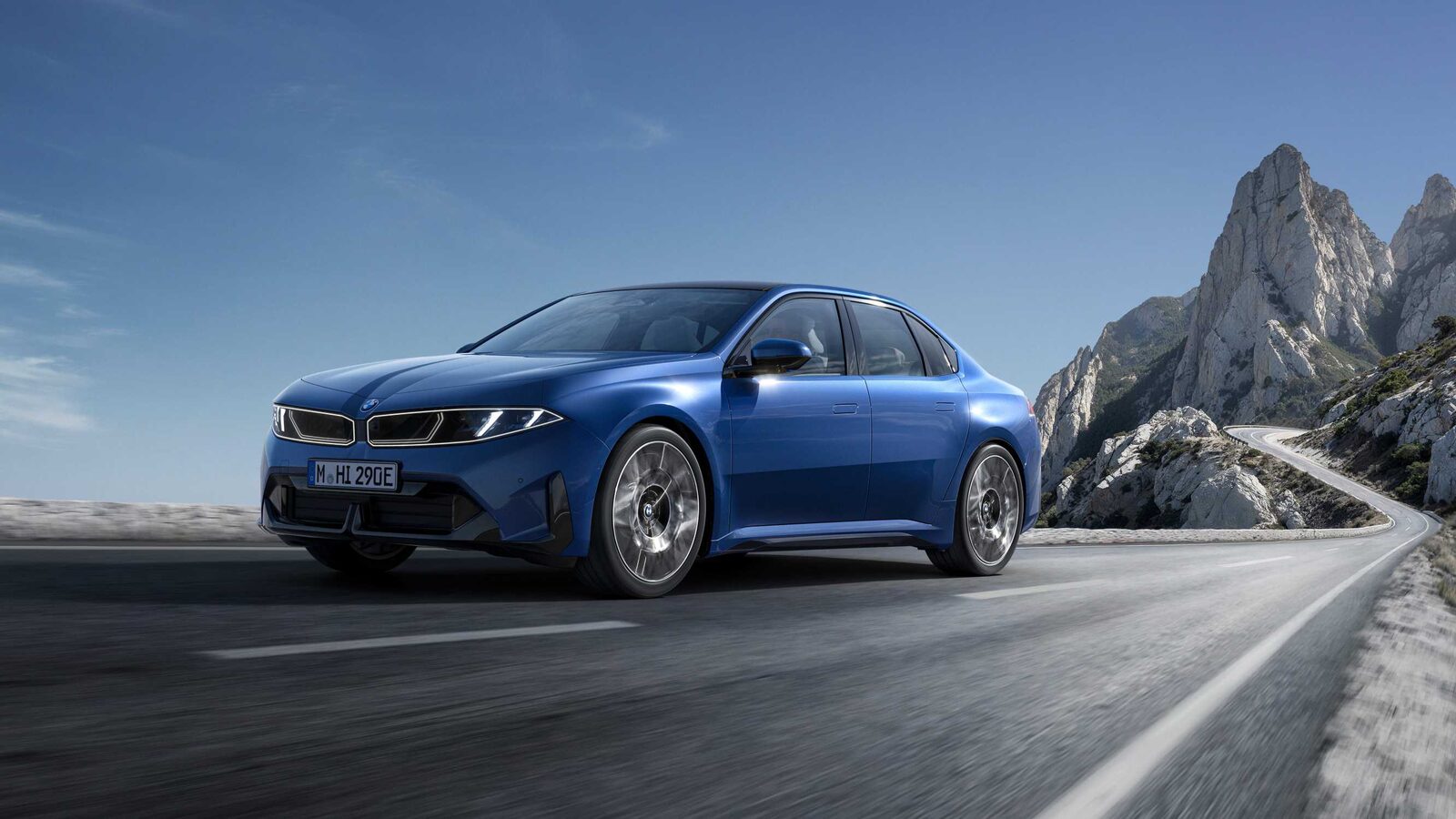 Blauer BMW i3 der Neuen Klasse fährt auf einer Küstenstraße, im Hintergrund helle Felsberge