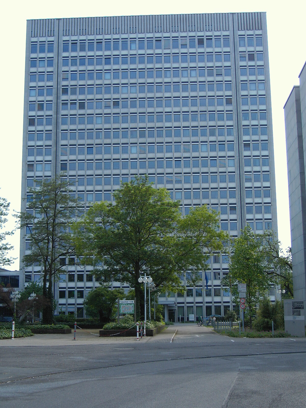 Das Hochhaus Tulpenfeld 4 in Bonn, Sitz der Bundesnetzagentur, von vorne mit Bäumen im Vordergrund