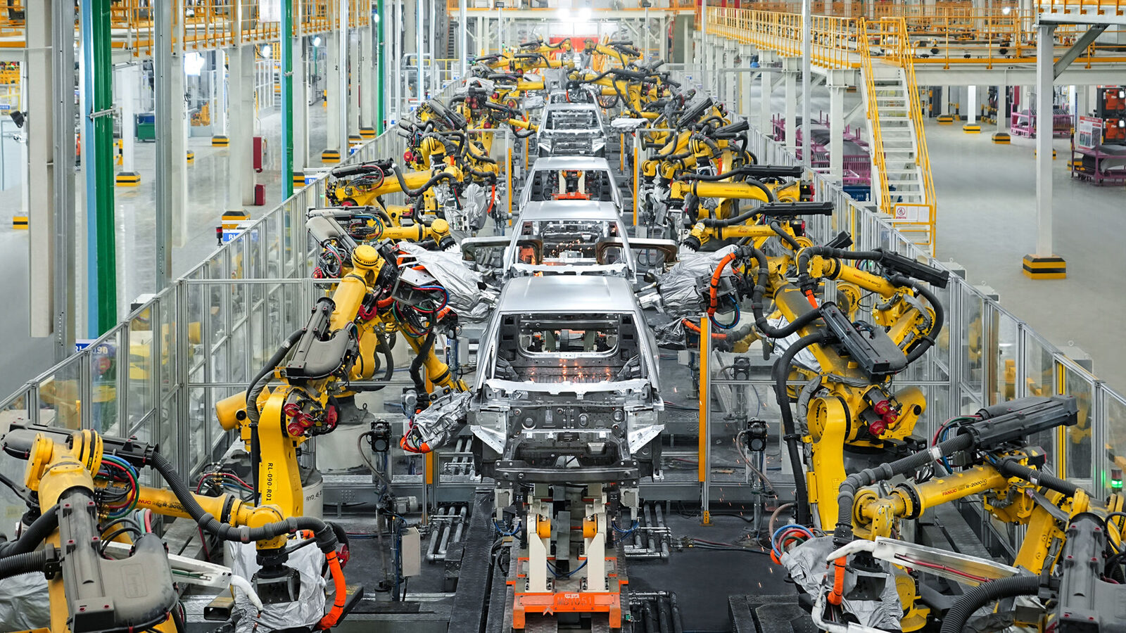 BYD fabrikasında sarı kaynak robotlarının arasında ilerleyen araç gövdeleri (BYD'nin Macaristan fabrika duyurusundaki basın görseli)