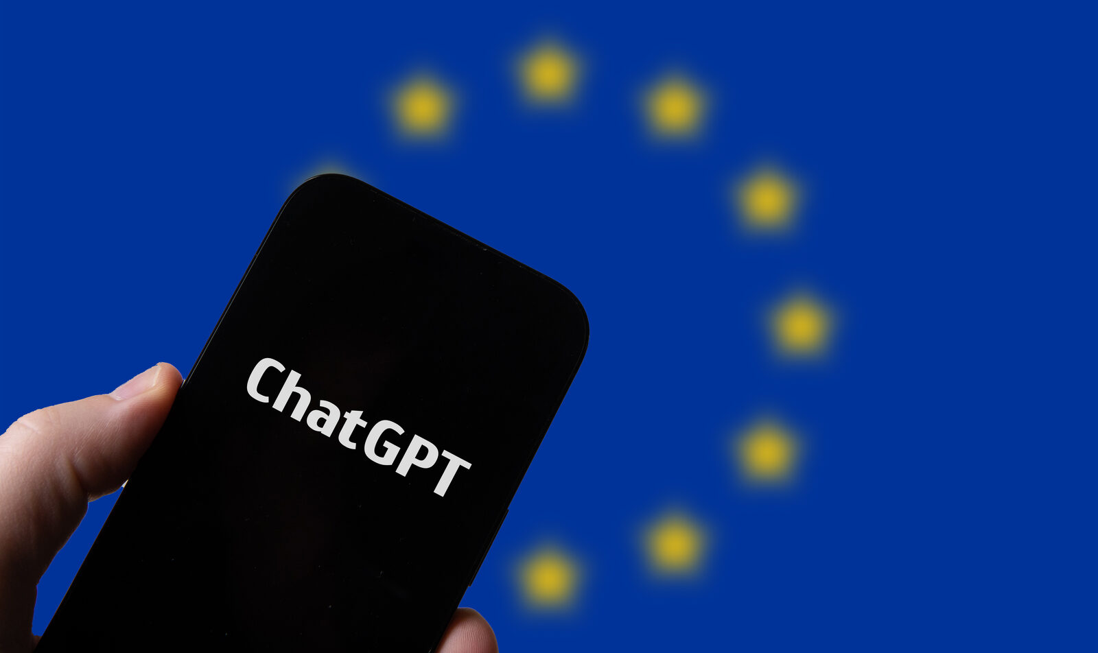 Hand hält ein Smartphone mit ChatGPT-Schriftzug vor einer Europaflagge