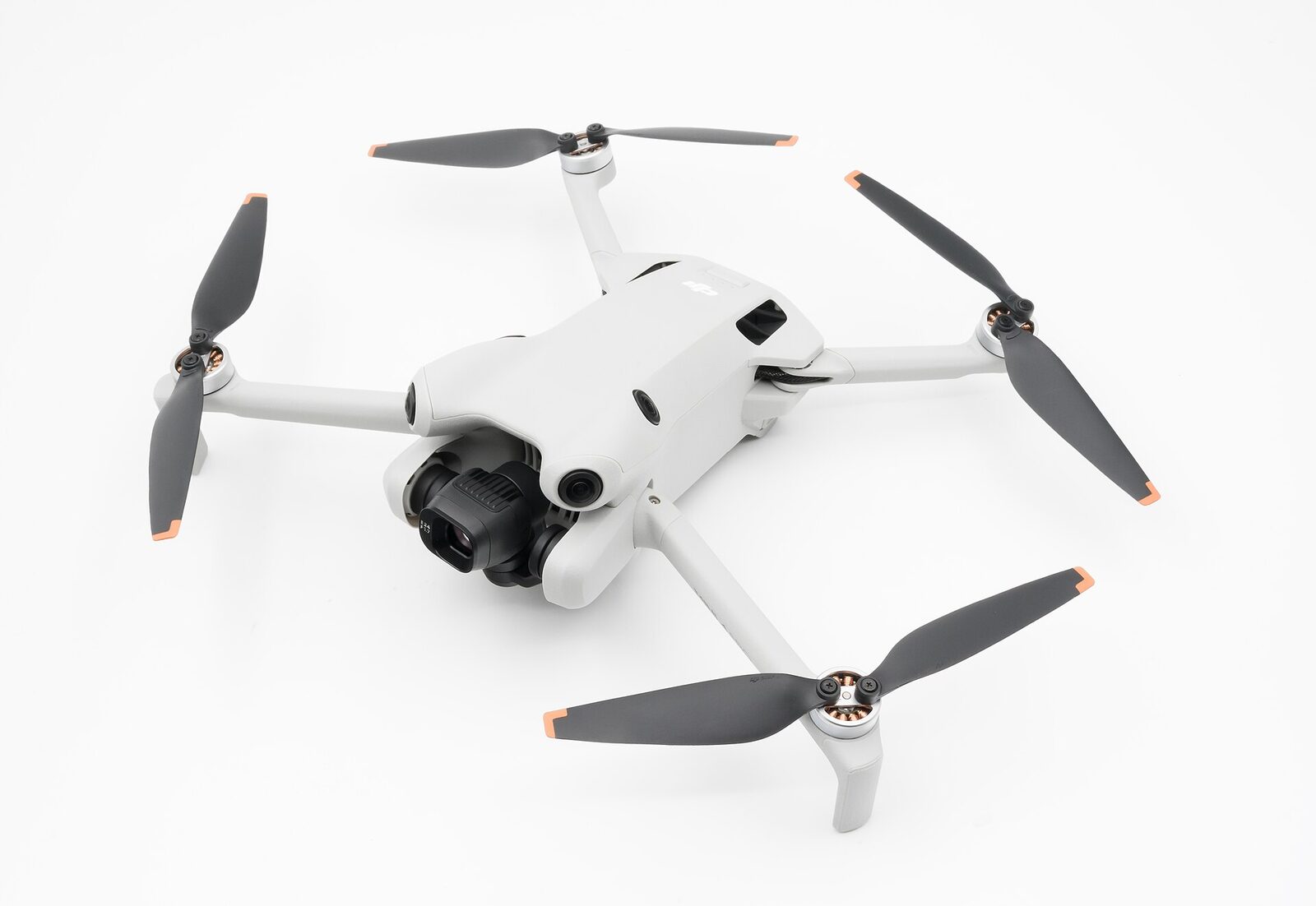 Beyaz zemin üzerinde pervaneleri açık DJI Mini 4 Pro drone