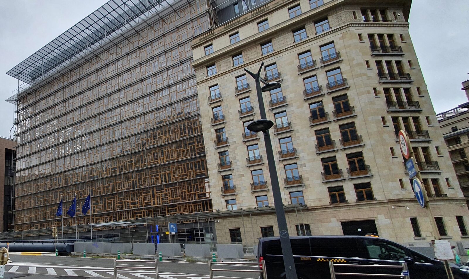 Das Europa-Gebäude des Rats der EU in Brüssel mit gläserner Fassade aus alten Holzfenstern neben dem denkmalgeschützten Altbau der Résidence Palace, davor EU-Flaggen