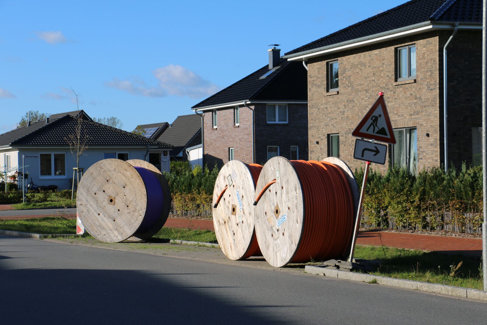 Kabeltrommeln mit orangefarbenen und violetten Leerrohren für den Glasfaserausbau an einer Straße in einem Wohngebiet