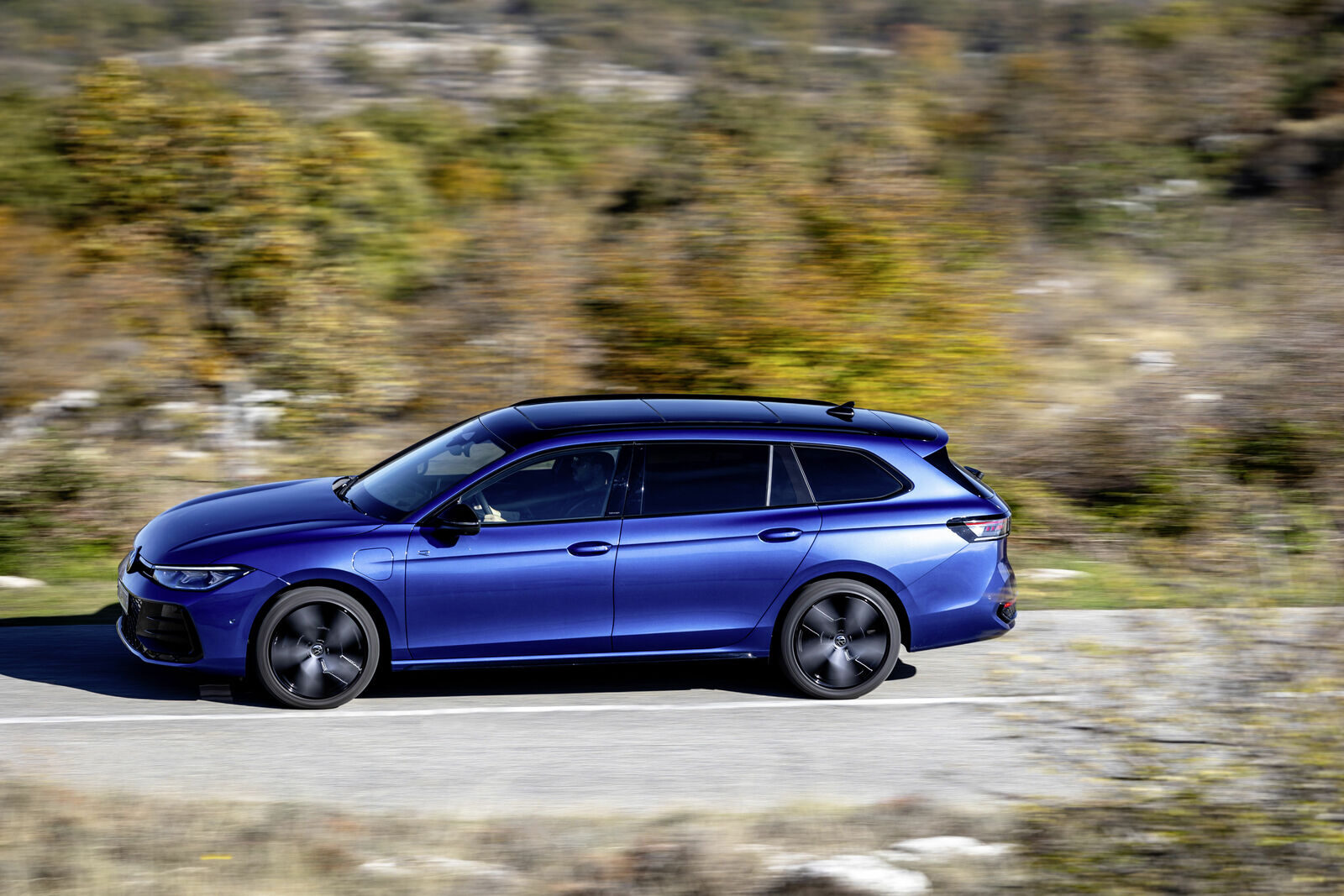 Mavi Volkswagen Passat Variant, yolda hareket halinde yandan görünüm