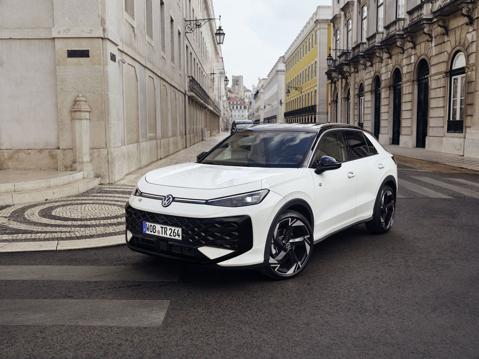 Beyaz yeni Volkswagen T-Roc, taş döşeli bir sokakta önden-yandan görünüm