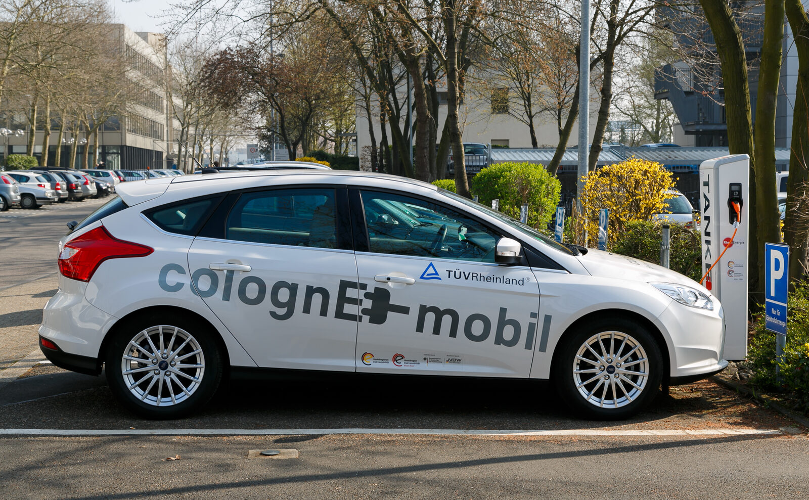 Ein weißes Elektroauto lädt an einer Ladesäule auf einem Parkplatz in Köln