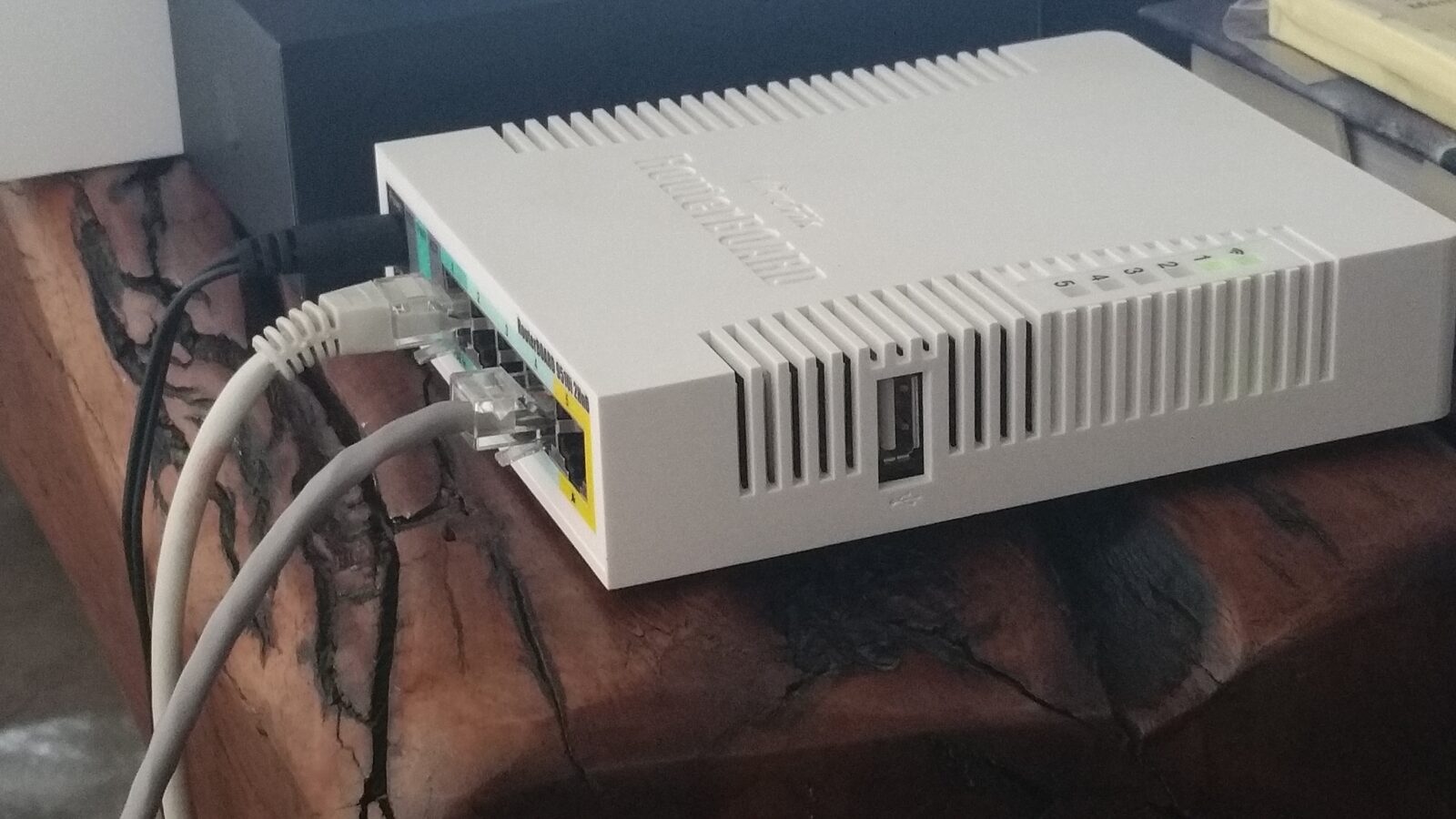 Weißer MikroTik RouterBOARD RB951Ui-2HnD mit angeschlossenen Netzwerkkabeln auf einem Holztisch (Foto: Deavmi, CC BY-SA)