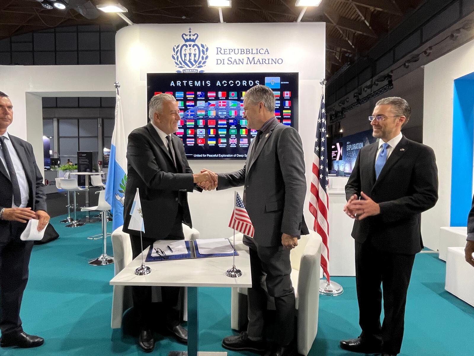 Il segretario di Stato sammarinese Rossano Fabbri stringe la mano al rappresentante NASA in Europa Gregory Mann davanti al pannello degli Accordi Artemis