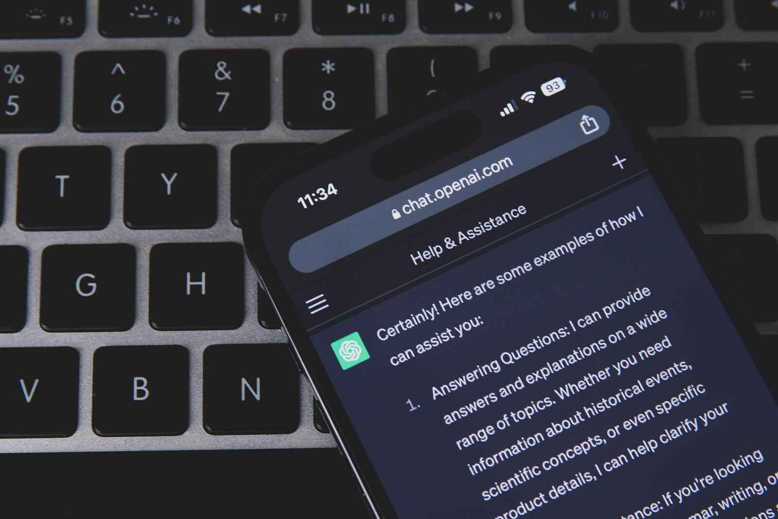 Smartphone mit geöffneter Chatbot-App liegt auf einer Computertastatur