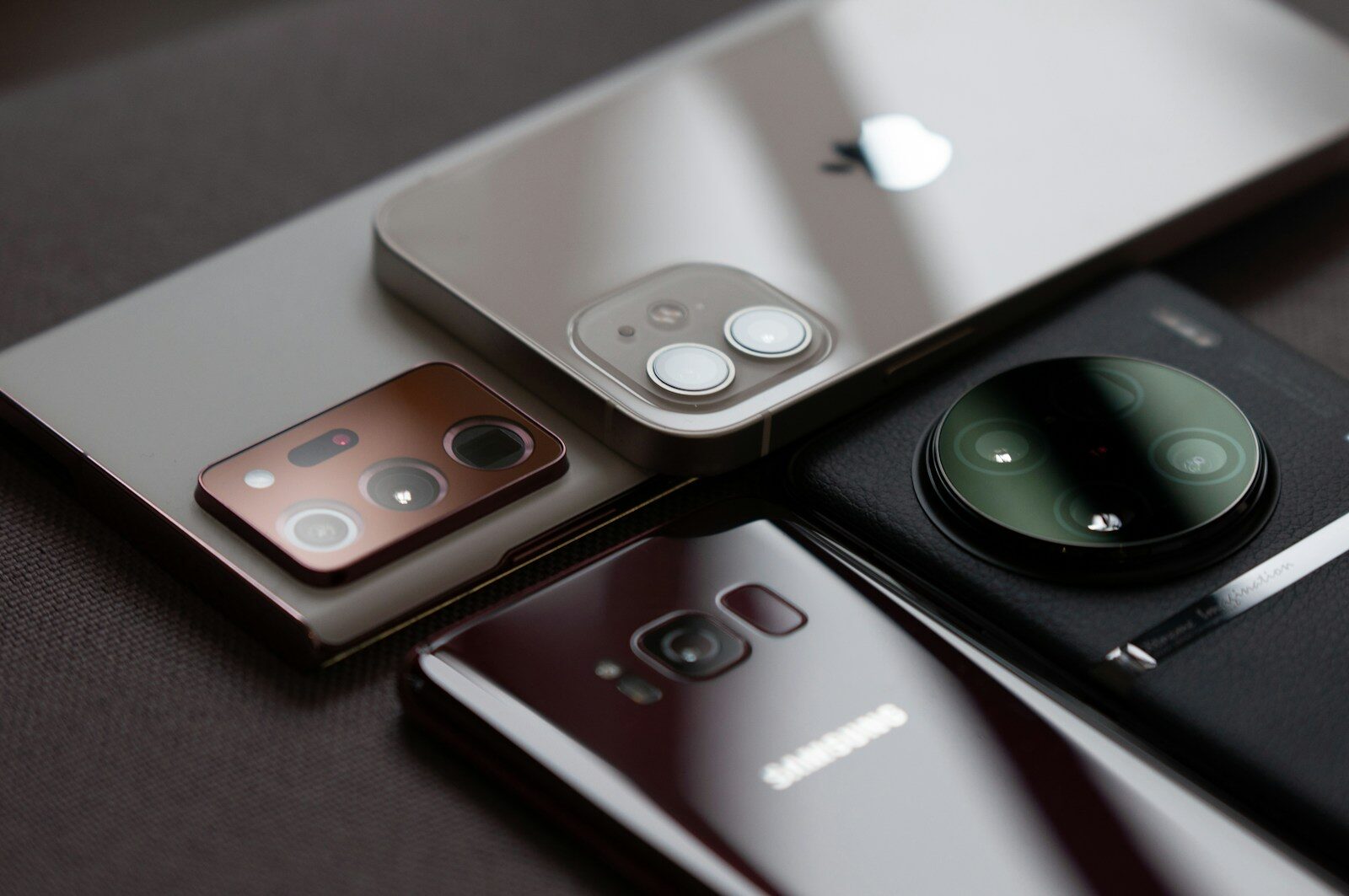 Mehrere ältere Smartphones von Apple, Samsung und Xiaomi liegen mit den Kameras nach oben auf einem Tisch