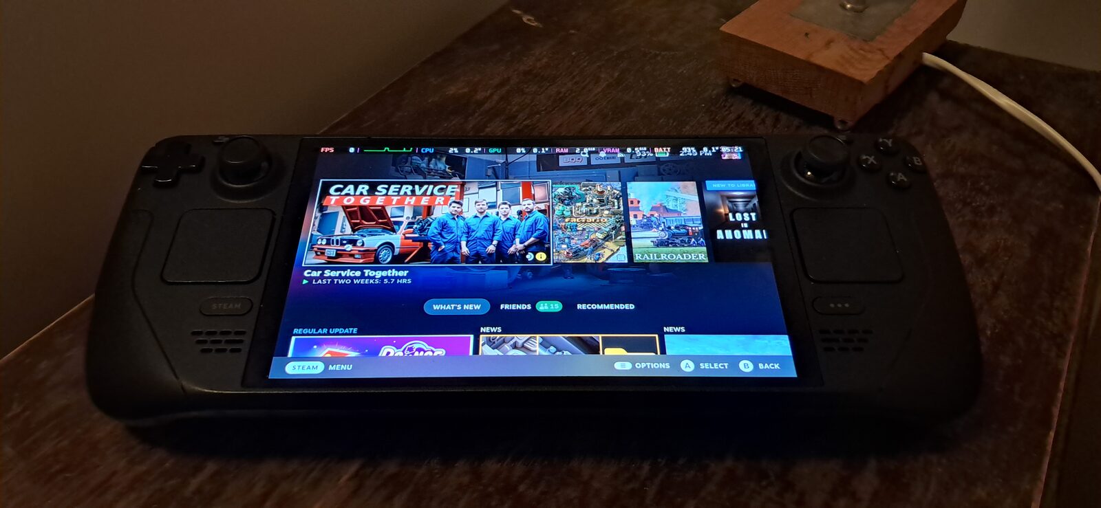 Masa üzerinde duran Steam Deck OLED el konsolunun ekranında Steam ana menüsü ve oyun kütüphanesi