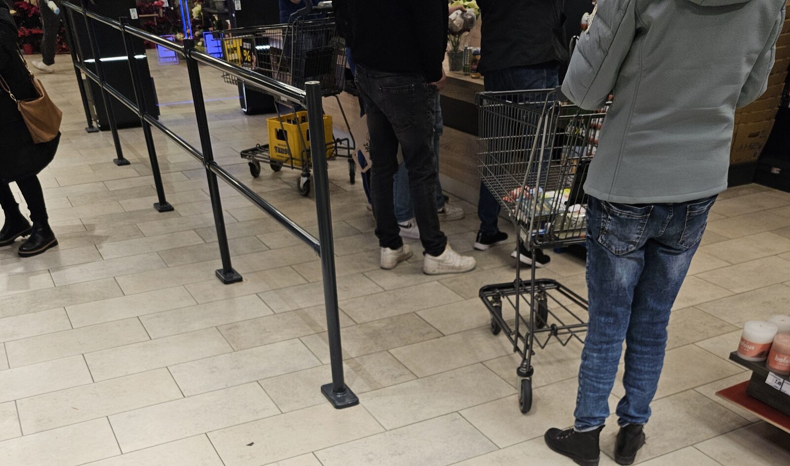 Kundinnen und Kunden mit Einkaufswagen warten im Kassenbereich eines Supermarkts in Baden-Württemberg