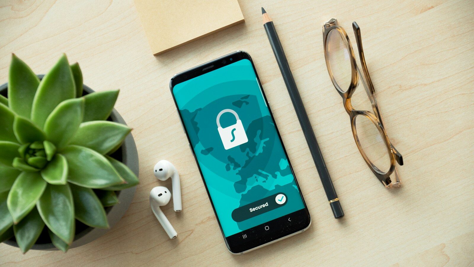 Ahşap masada ekranında kilit simgesi bulunan akıllı telefon, yanında kulaklık ve gözlük