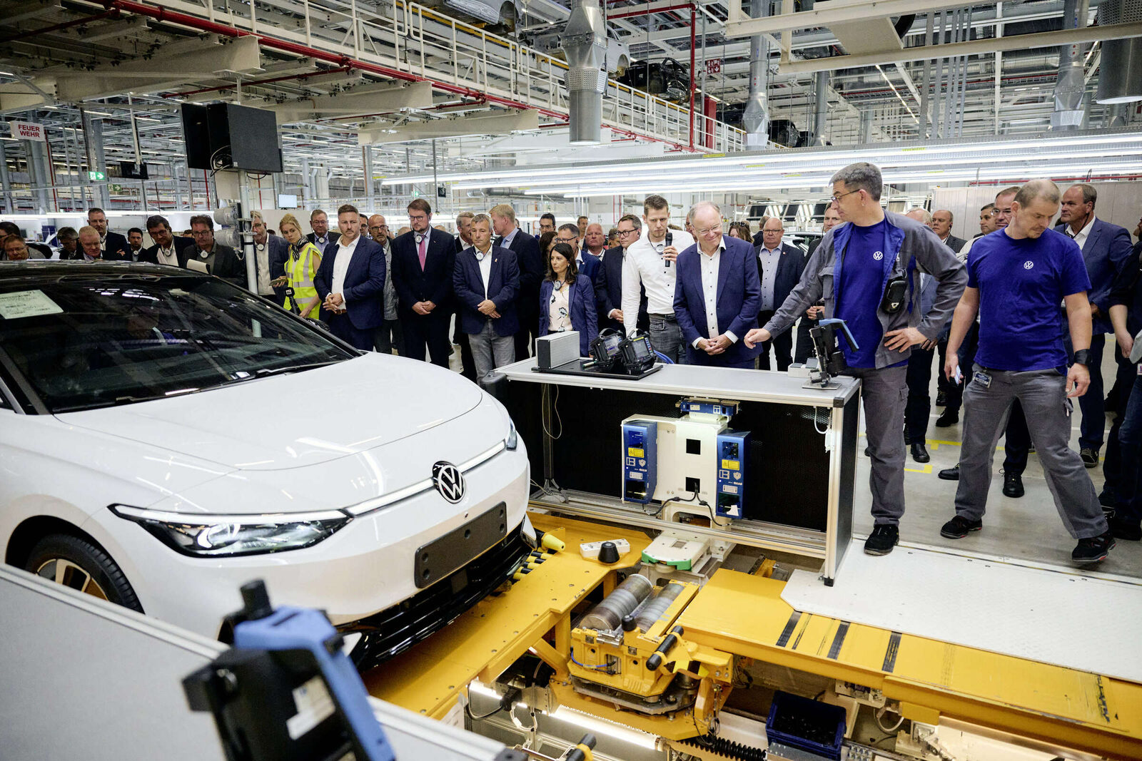 Bild: Volkswagen (Archivbild vom Produktionsstart des ID.7, 2023) Ein weißer VW ID.7 auf der Montagelinie im Werk Emden, dahinter Mitarbeitende und Gäste