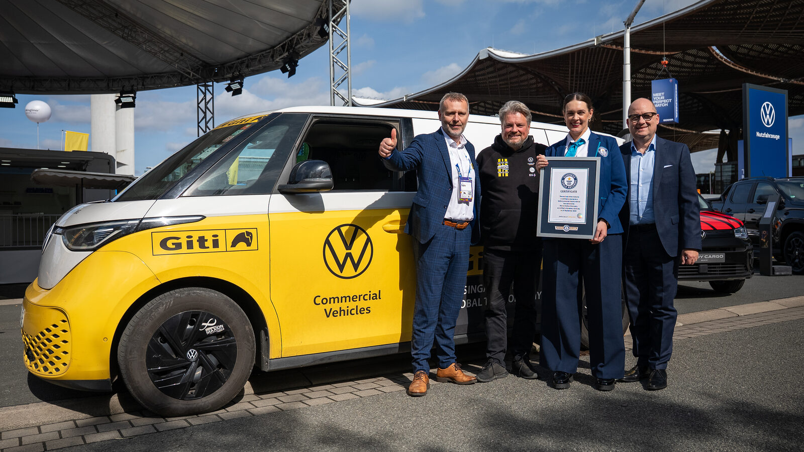 Sarı-beyaz Volkswagen ID. Buzz'ın önünde Guinness Dünya Rekorları sertifikasını tutan Rainer Zietlow ve yöneticiler