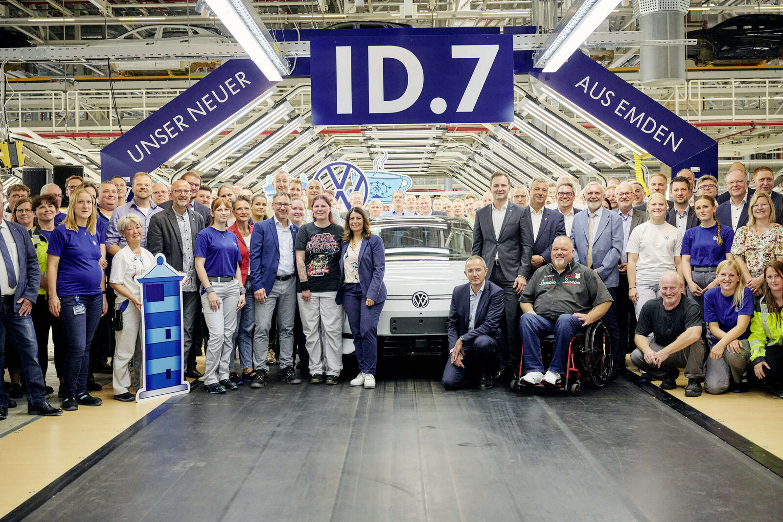 Belegschaft des VW-Werks Emden vor einem weißen ID.7 unter einem Banner mit der Aufschrift „Unser neuer ID.7 aus Emden“
