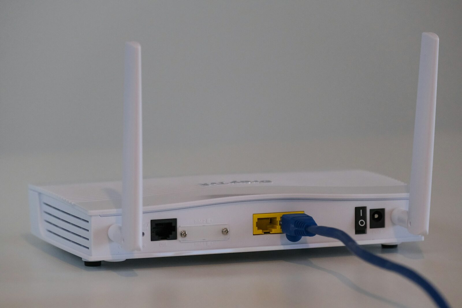 İki antenli beyaz bir Wi-Fi modemin arkadan görünümü, portuna mavi Ethernet kablosu takılı