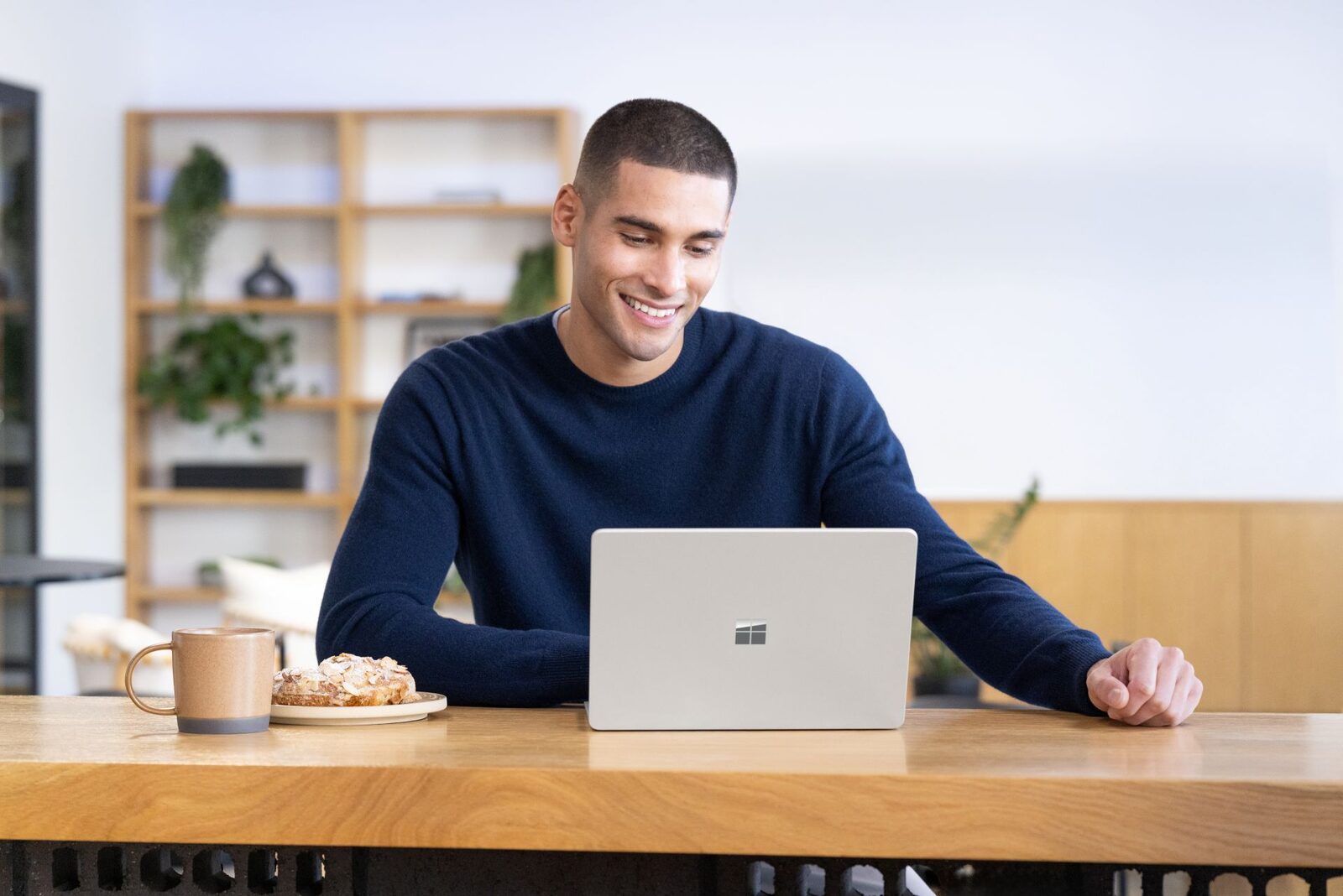 Lächelnde Person arbeitet in einem Café an einem silbernen Surface Laptop
