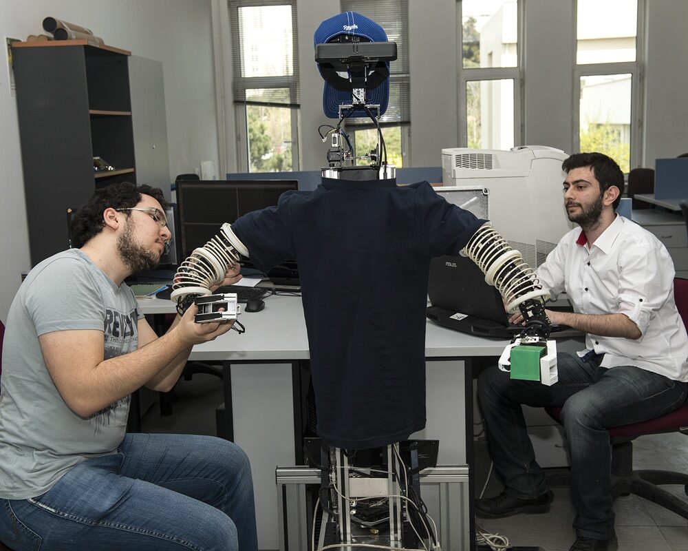 Üniversite laboratuvarında iki öğrenci insansı bir robotun kollarına sensörlü eldiven takıyor