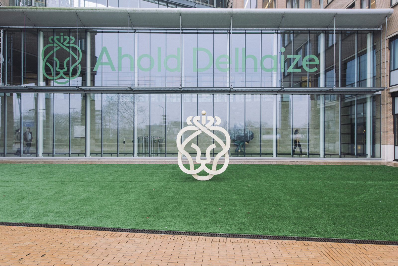 Glazen gevel van het hoofdkantoor van Ahold Delhaize in Zaandam met het leeuwenlogo op een grasveld ervoor