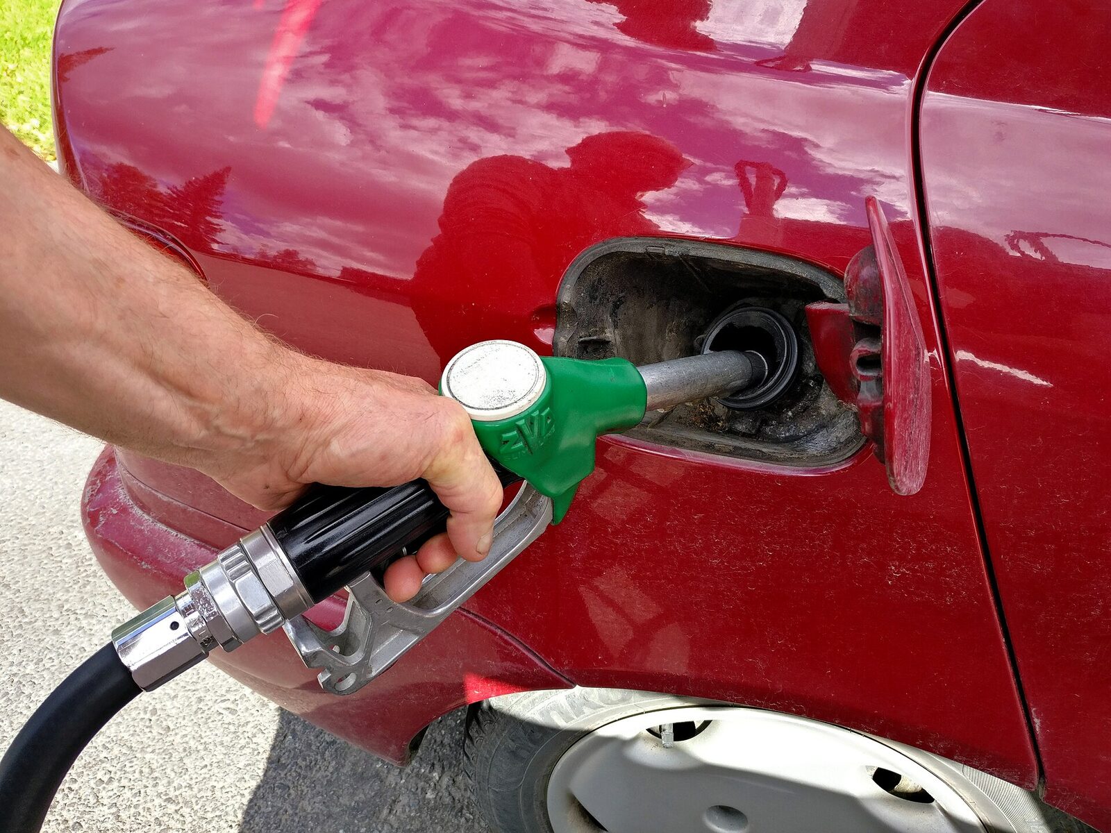Kırmızı bir otomobilin deposuna yeşil tabancalı pompayla yakıt dolduran el