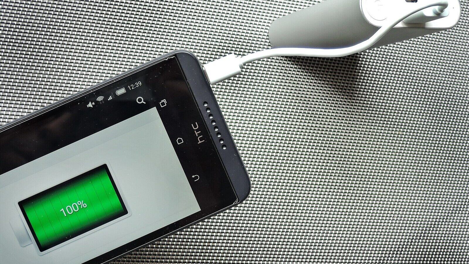 Smartphone mit 100-Prozent-Ladeanzeige hängt per USB-Kabel an einer Powerbank
