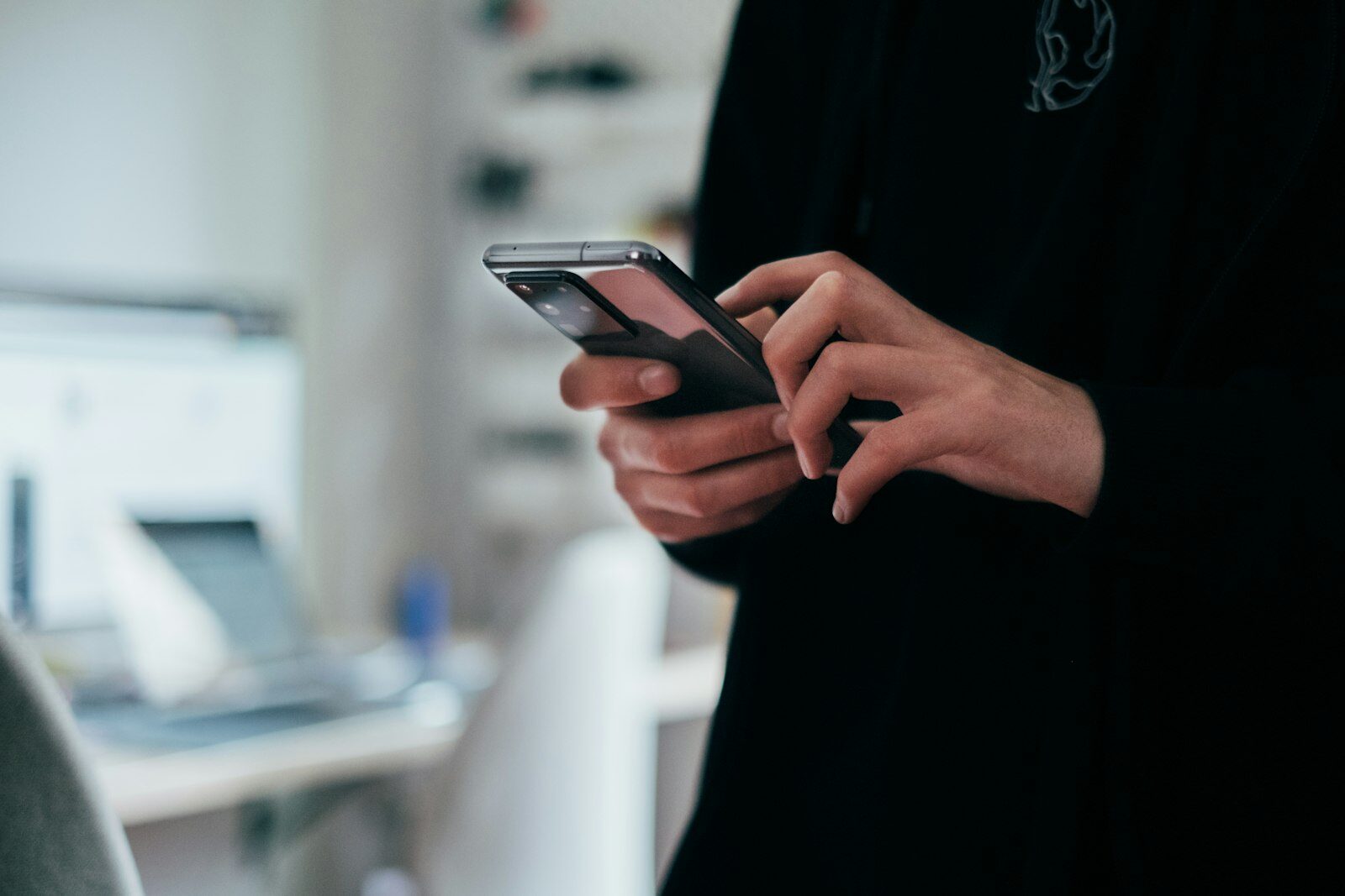 Siyah kazaklı bir kişinin elinde arka kamerası görünen Android akıllı telefon