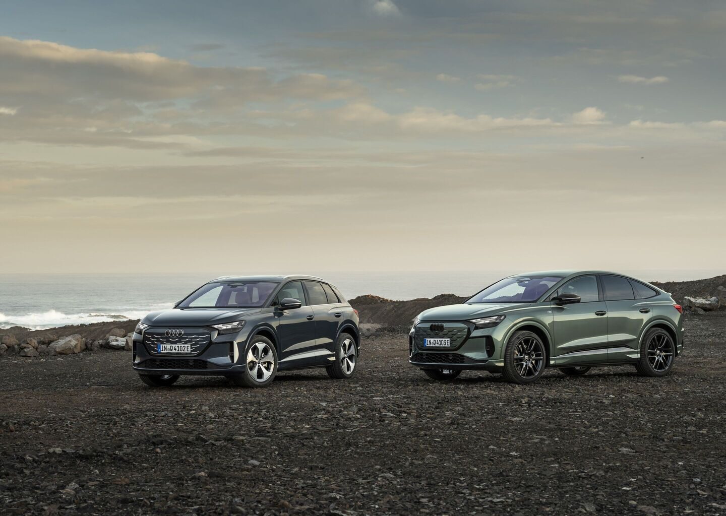 Deniz kıyısında yan yana duran koyu gri Audi Q4 SUV e-tron ve yeşil Audi Q4 Sportback e-tron
