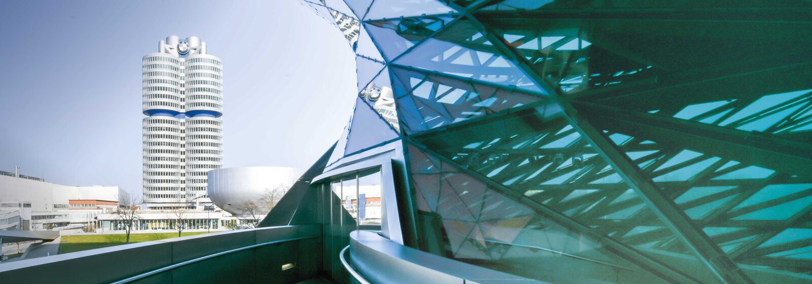 Der BMW-Vierzylinder-Turm und die schalenförmige BMW-Museum-Kuppel in München, rechts im Vordergrund die gläserne Dachkonstruktion der BMW Welt