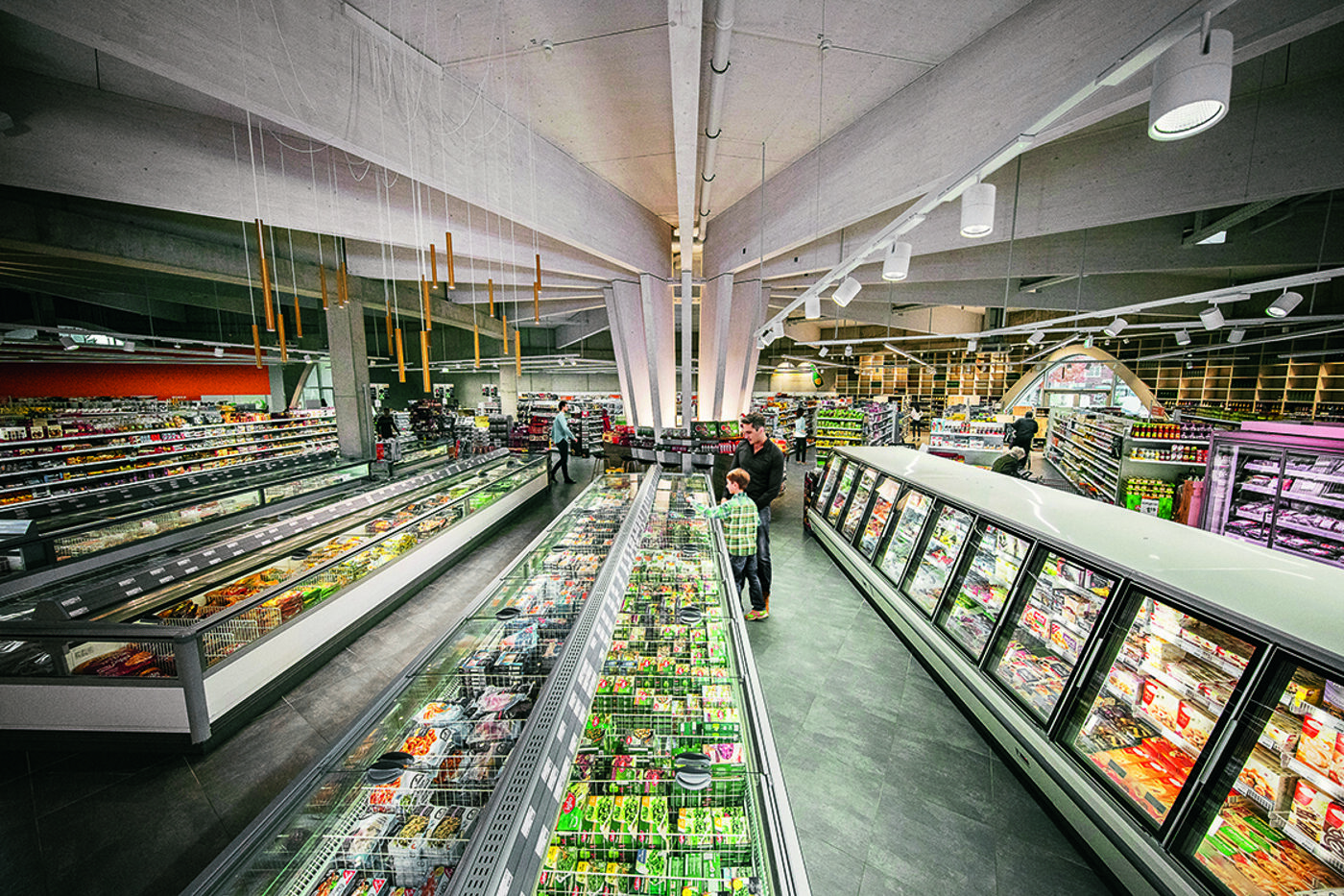 Corsia di un supermercato con lunghi banchi frigo e congelatori a vetro pieni di prodotti surgelati