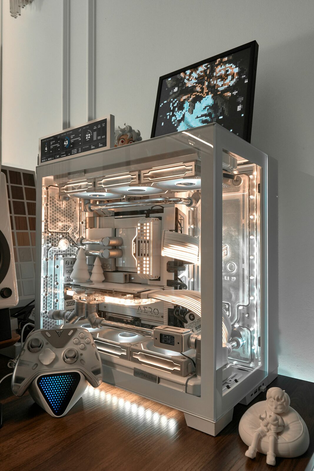 Weißer Gaming-PC mit Glasseitenteil, Wasserkühlung und Beleuchtung auf einem Schreibtisch, daneben ein Controller
