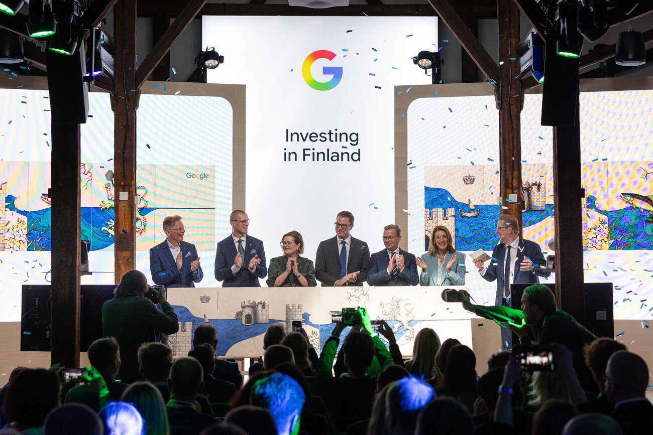 Zeven mensen applaudisseren op een podium in Helsinki voor een scherm met het Google-logo en de tekst Investing in Finland