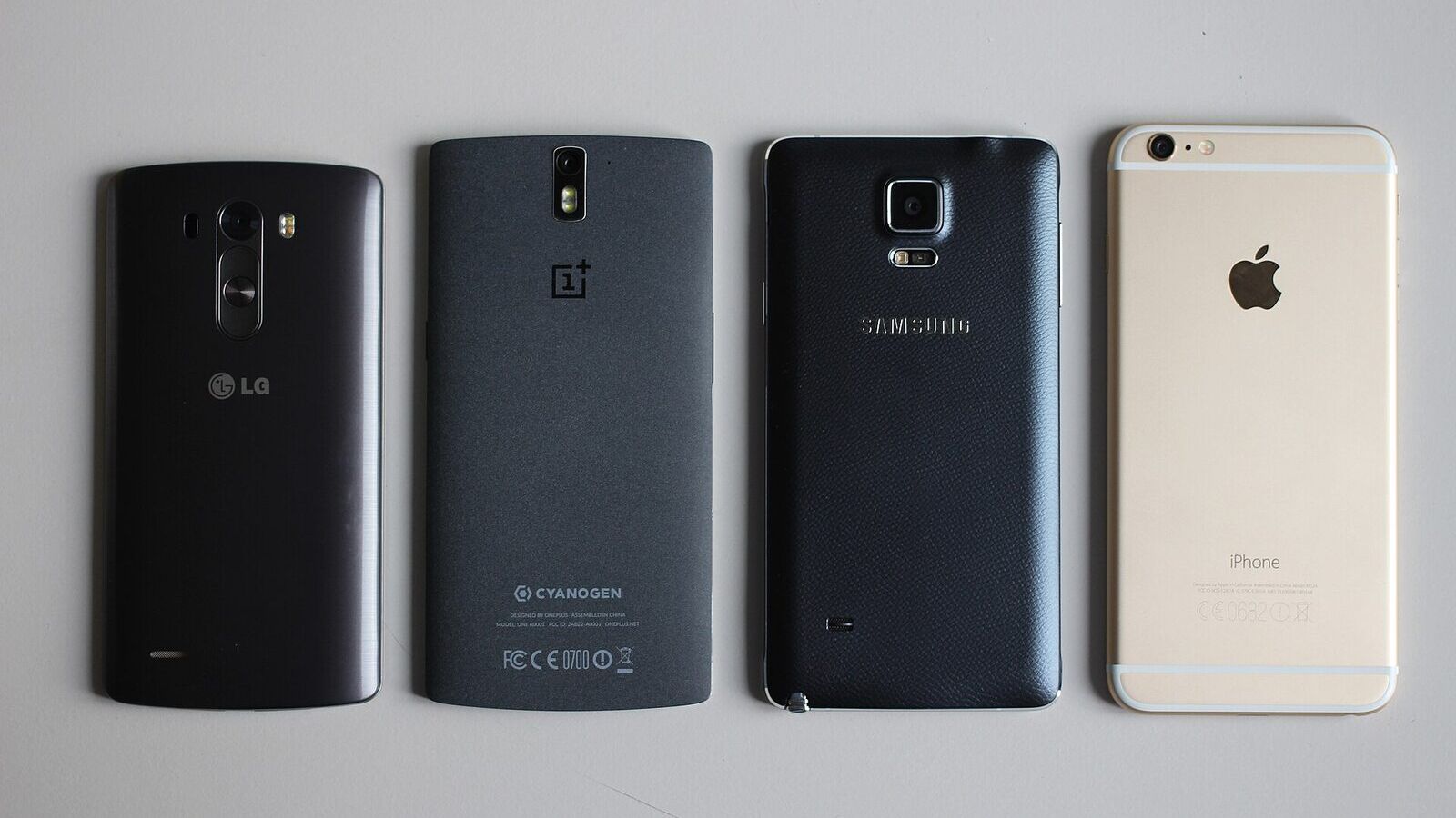 Arka yüzleri görünen LG, OnePlus ve Samsung Android telefonlar ile bir iPhone yan yana