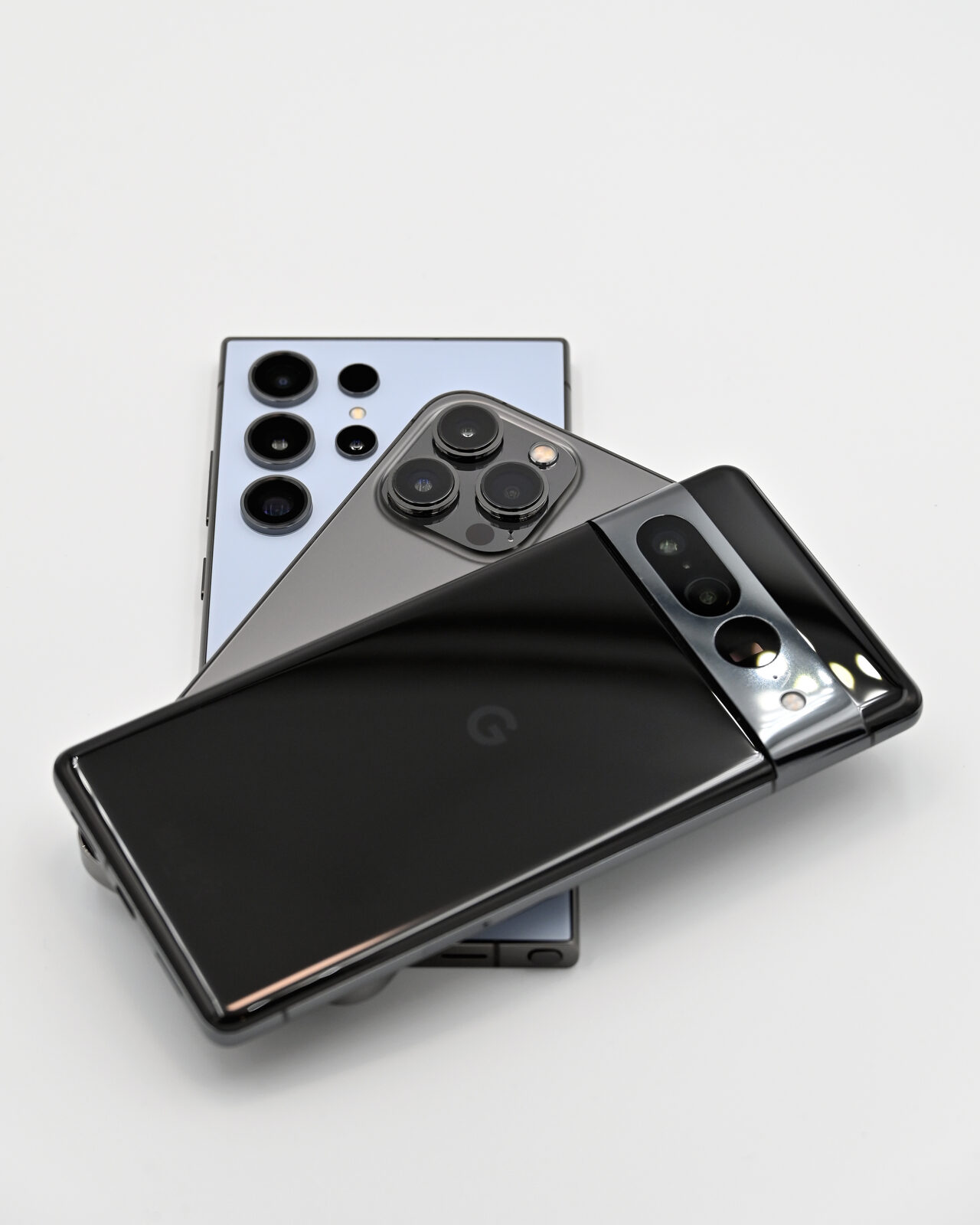 Samsung Galaxy S24 Ultra, iPhone 13 Pro und Google Pixel 7 Pro liegen übereinander, Rückseiten mit Kameras sichtbar