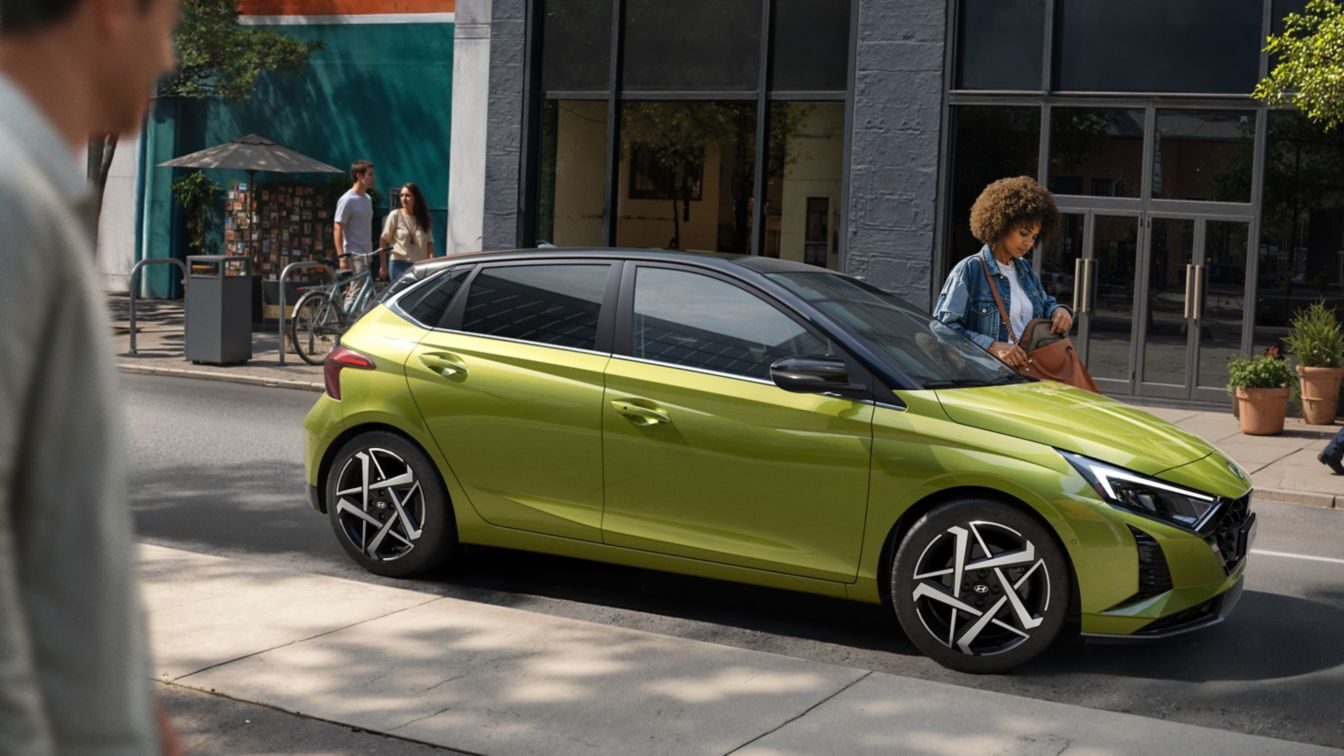 Sarı-yeşil Hyundai i20, bir mağaza önündeki caddede yandan görünüm
