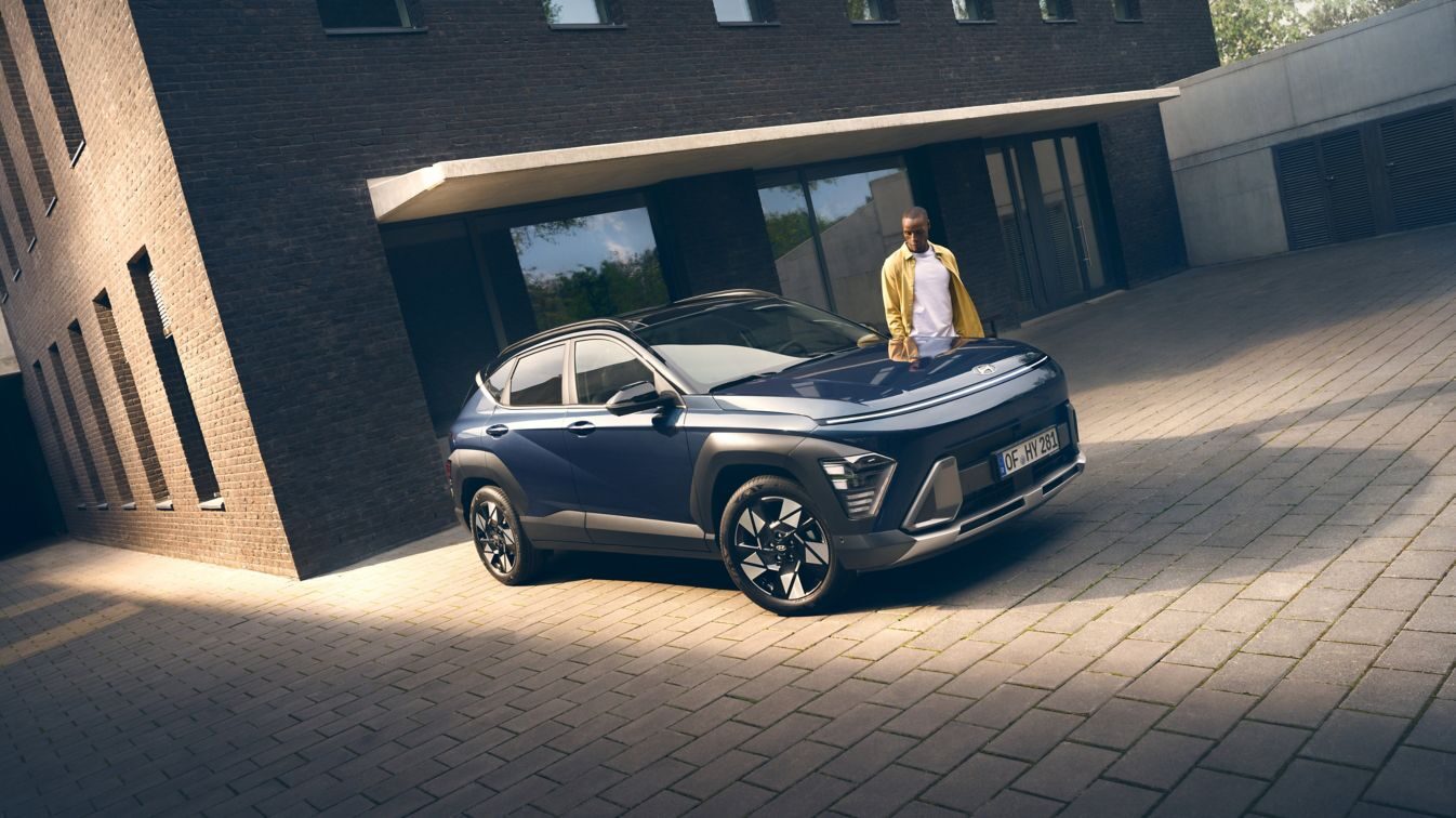 Lacivert Hyundai Kona, tuğla bir binanın önünde önden çapraz görünüm