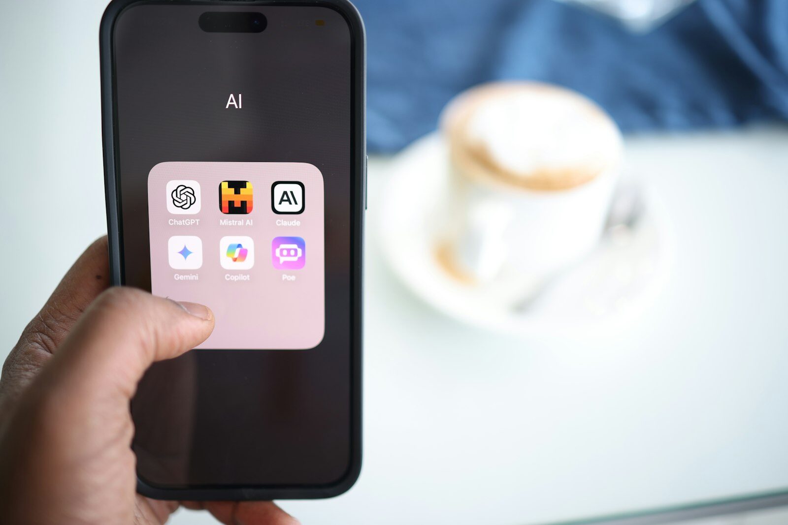 Hand hält ein Smartphone mit einem App-Ordner „AI“, darin ChatGPT, Gemini, Copilot und weitere KI-Apps