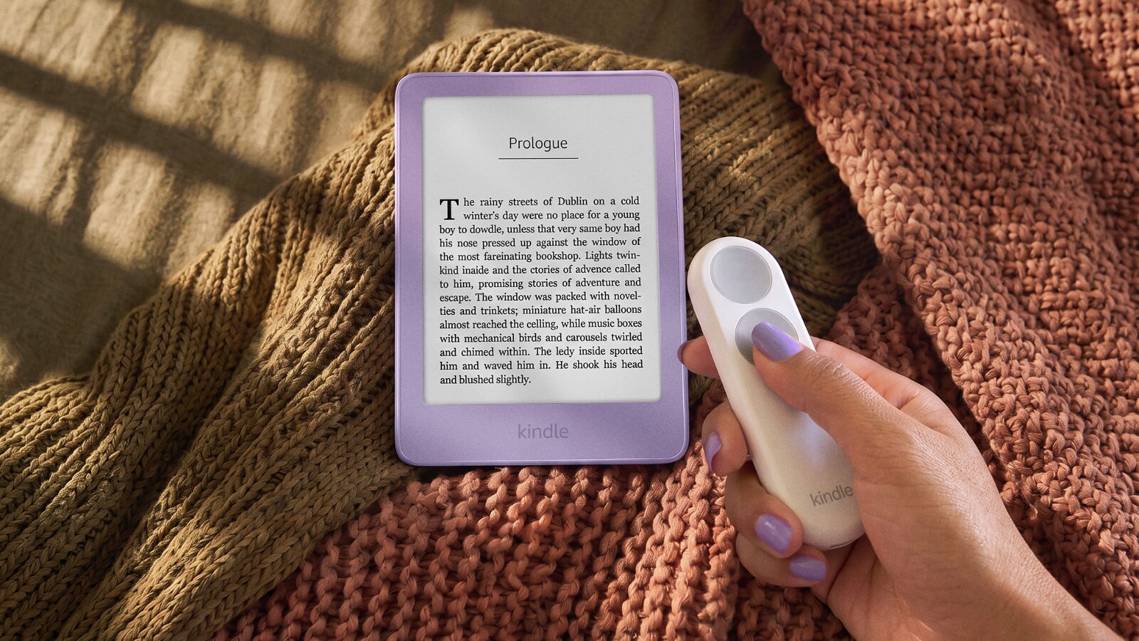 Örgü battaniye üzerinde duran mor (Ube) renkli yeni Kindle ve elde tutulan beyaz Kindle Click sayfa çevirme kumandası