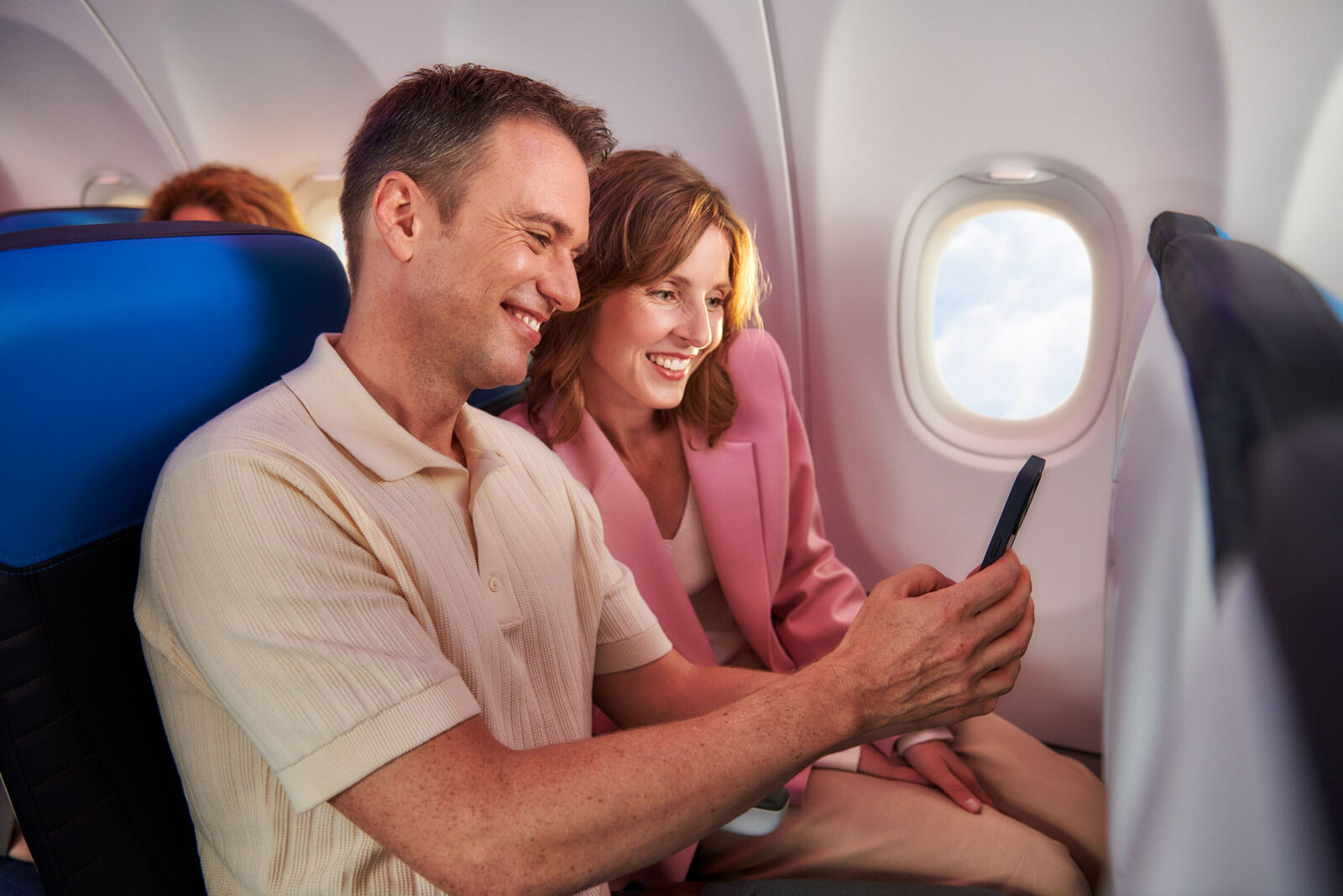 Twee passagiers kijken lachend samen naar een smartphone aan boord van een KLM-toestel