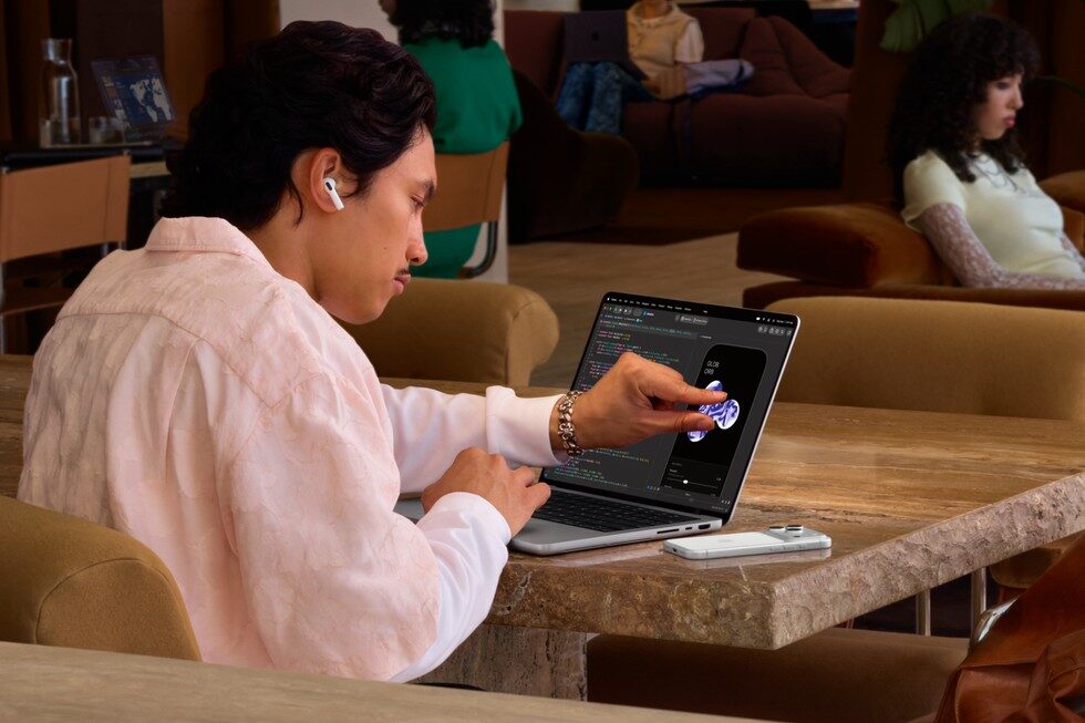 Bild: Apple Ein Mann tippt in einem Café auf das Display eines MacBook Pro mit PROLED XDR Display