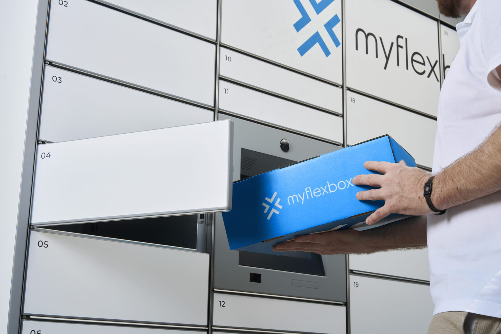 Ein Paket in einem blauen Myflexbox-Karton wird in ein geöffnetes Fach einer weißen Myflexbox-Paketstation gelegt