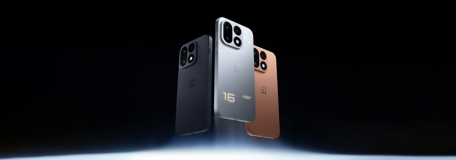 Siyah, gümüş ve turuncu renkteki üç OnePlus 16 arkadan görünüyor; gümüş modelin arkasında ışıklı 16 yazısı var