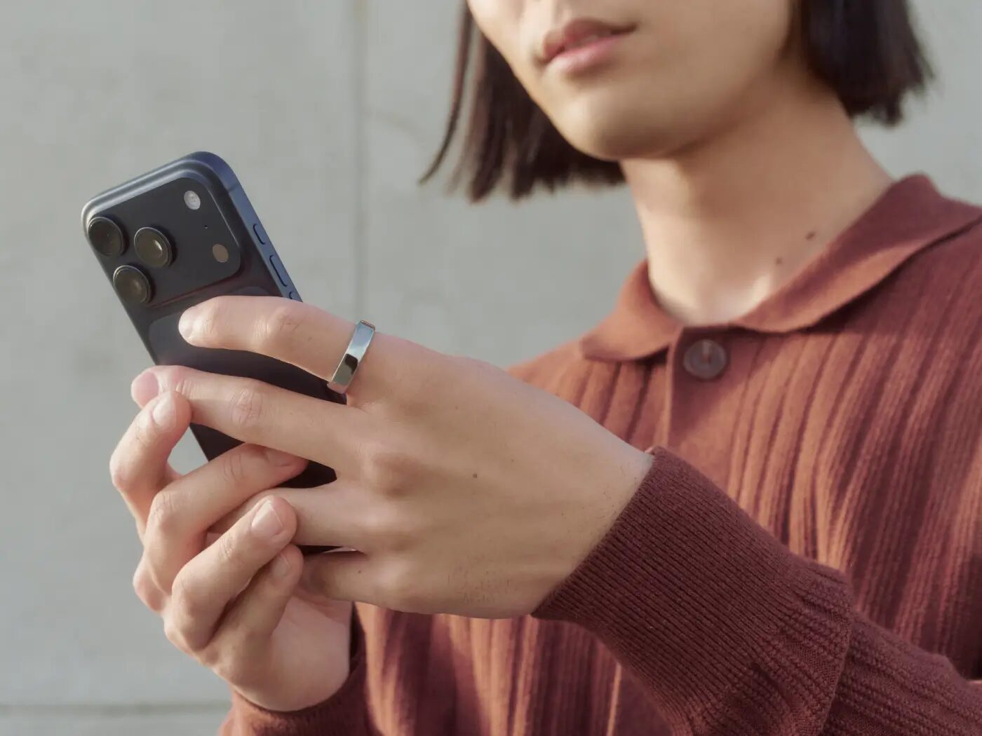 Person mit silbernem Oura Ring am Zeigefinger hält ein Smartphone in der Hand