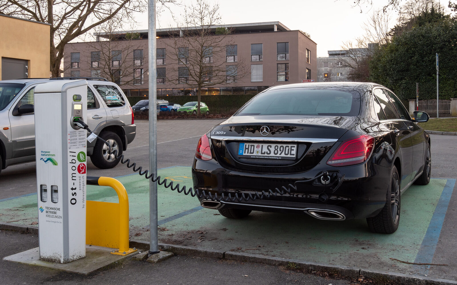 Şarj kablosu takılı siyah bir Mercedes-Benz C 300 e plug-in hibrit, halka açık bir şarj istasyonunda