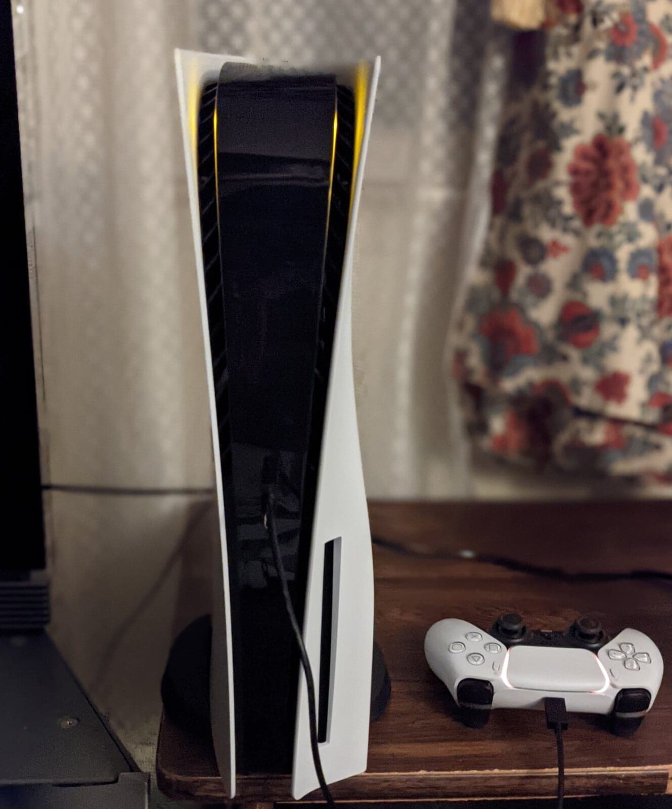 Een witte PlayStation 5 staat rechtop op een houten kast, met een DualSense-controller ernaast