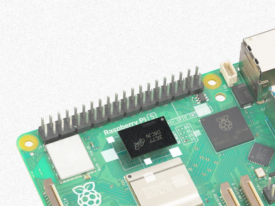 Nahaufnahme einer grünen Raspberry-Pi-5-Platine mit dem schwarzen Speicherchip in der Mitte, daneben GPIO-Stiftleiste und Raspberry-Logo