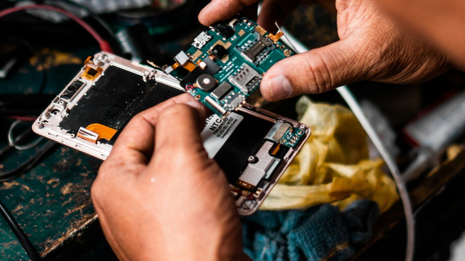 Mani di un tecnico che smontano uno smartphone Android ed estraggono la scheda madre su un banco da lavoro
